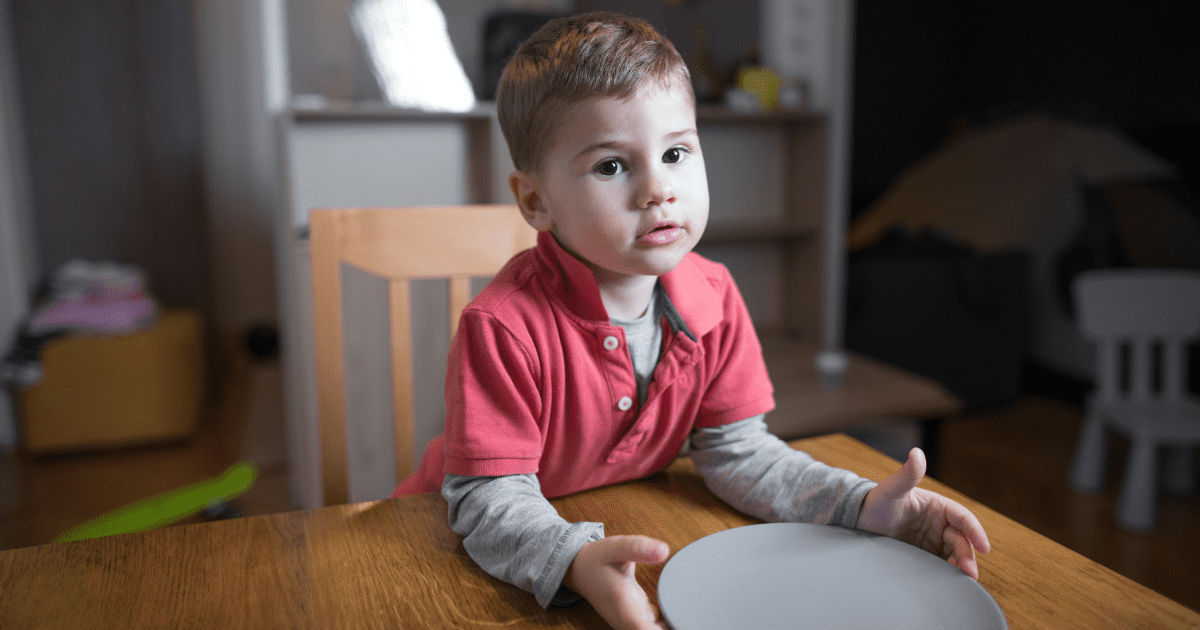 young boy sitting at kitchen table with an empty plate