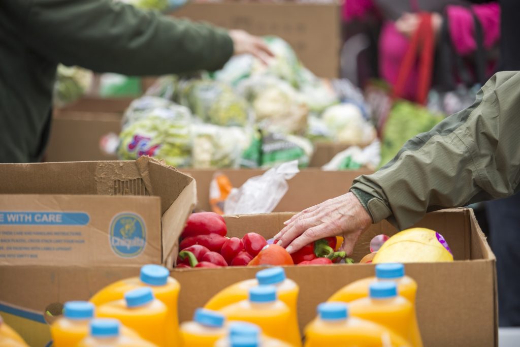 Image of table full of food in boxes, you can see volunteers arranging cauliflower and red peppers.