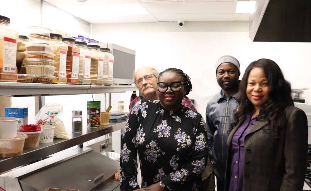 NACCO founder and three board members stand in the Chrispy African market kitchen by dry food rack.