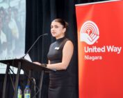 Isha Dadhwal, program coordinator, at the podium, speaking at International Women’s Day event about the benefit and importance of earning a living wage.